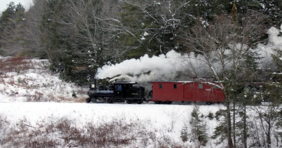 A narrow gauge steam train dashes through the snow covered fields and forest at the WW&F Railway Museum in Alna, Maine.